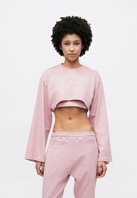 Világos rózsaszín, rövidített pul�óver hosszú ujjakkal és hímzett részletekkel. Párosítva hozzáillő rózsaszín melegítőnadrággal, melynek rugalmas derékrésze van.