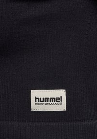 Black textured fabric with a white rectangular label stitched, displaying "hummel PERFORMANCE" in black text.