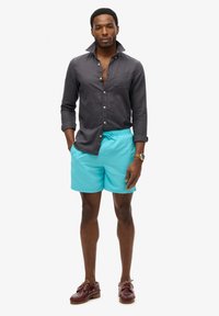 Shorts de bain bleu clair avec une taille élastique, assortis à une chemise boutonnée foncée et des chaussures bateau brunes. Tissu lisse, coupe décontractée.