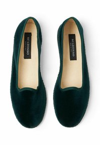 Scarpe slip-on in velluto verde scuro con punta arrotondata, collo elastico e interno in lino naturale. Presentano cuciture sottili lungo la suola.