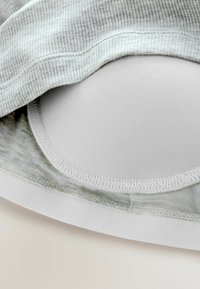 Gråstribet stofoverlay dækker en hvid, sømløs bh-kop. Kanterne er færdigbehandlet med pæne sting, hvilket fremhæver den glatte struktur og design.