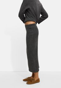 Sweter w kolorze węgla drzewnego z prążkowanej tkaniny oraz midi spódnica wykonana z miękkiej dzianiny, zestawione z brązowymi zamszowymi mokasynami z metalowymi oczkami.