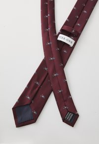 Cravate en soie bordeaux avec un motif de petites voitures, dotée d'une doublure sombre unie et d'étiquettes cousues au dos. Texture lisse avec un design étroit.
