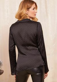 Blusa nera con pois bianchi, maniche lunghe e una texture morbida. Vestibilità impeccabile con colletto classico e orlo leggermente svasato.