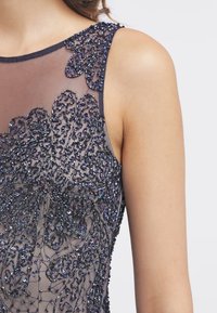 Beaded dress with sheer fabric, featuring intricate floral patterns in dark hues and shimmering sequins, highlighting a textured design.