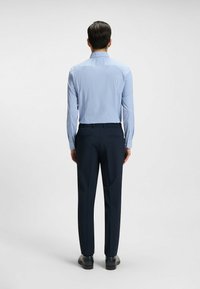 Camicia a maniche lunghe a quadri blu e bianchi con colletto appuntito, abbinata a pantaloni navy scuri e scarpe nere, vista da dietro.