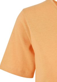 Lyhythihainen T-paita vaalean oranssia puuvillaa. Varusteena ribattu kaula-aukko ja ommeltu helma. Pehmeä rakenne tasaisella pinnalla.
