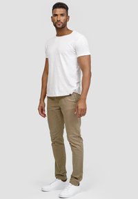 Camiseta blanca de manga corta, pantalones ajustados marrón claro y zapatillas blancas. La tela parece suave, con un diseño clásico y detalles mínimos.