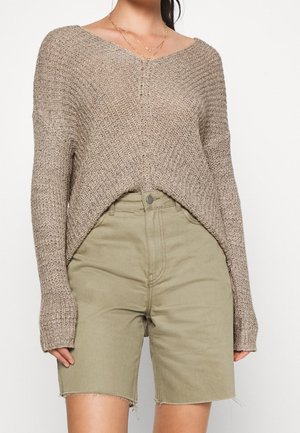 Maglione lavorato a maglia beige con scollatura a V, spalle cadenti e vestibilità ampia. Abbinato a pantaloni corti verde oliva con bordi sfilacciati.