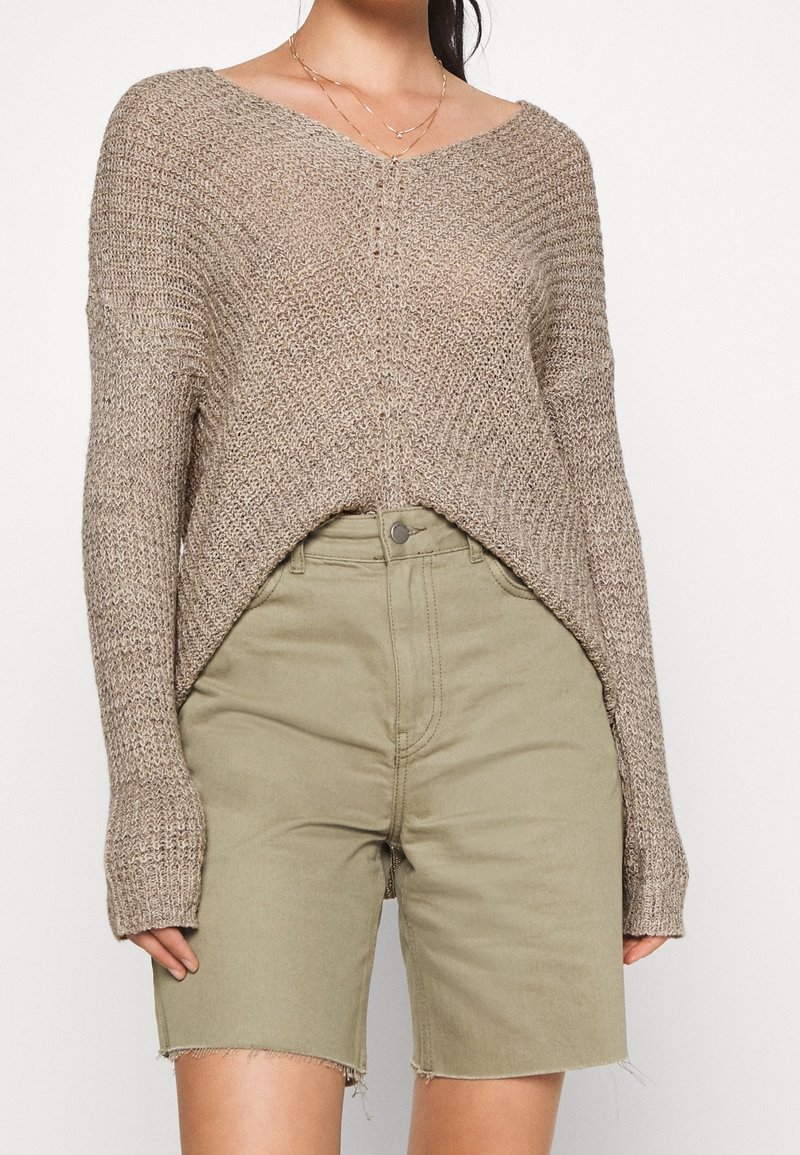 Beige stickad tröja med V-ringning, sänkta axlar och en lös passform. Matchas med olivgröna shorts med fransade kanter.