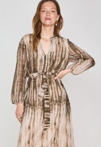 Abito lungo e leggero in beige con un motivo astratto marrone, dotato di maniche lunghe, scollo a V e vita con nastro per definire la forma.