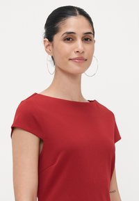 Rød kjole med korte ermer, rund hals og tettsittende design. Glatt tekstur, minimale sømmer og subtile side detaljer.