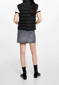 Svart vadderad väst utan ärmar med hög krage. Kombinerad med en grå jeanskjol, svarta ankelstövlar och mörka strumpor. Enkel design utan mönster.