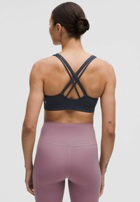 Sujetador deportivo negro con tirantes cruzados, textura suave y un diseño ajustado. Combinado con leggings de cintura alta en un suave tono rosa.