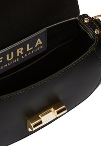 Interieur van een zwarte leren tas met een gouden metalen sluiting en stiksels. Bevat een merklabel "FURLA" in goud op een marineblauwe achtergrond.