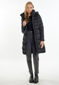 Sort pufferjakke med hætte, med vandret quiltet design, frontlynlås og sidelommer. Kombineret med mørkegrå jeans og sorte støvler.
