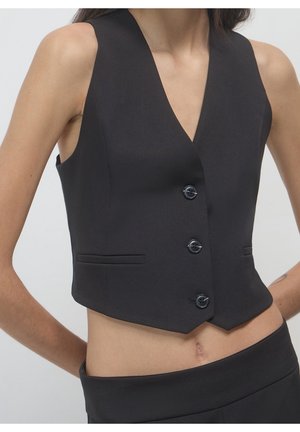 Chaleco corto negro sin mangas con tres botones y dobladillo en muesca, llevado sobre el abdomen descubierto, combinado con pantalones de cintura alta a juego.