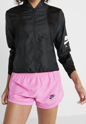 Schwarze Nike Zip-Jacke mit Netzpaneelen und langen Ärmeln, kombiniert mit pinken Sportshorts, die ein Logo und Netzbesatz haben.