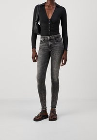 Bodysuit negro de manga larga con detalles de botones, combinado con jeans skinny gris desgastados. Se lleva con sandalias negras de tiras.