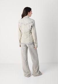 Giacca di jeans in grigio sbiadito, con colletto strutturato, dettaglio sulla schiena e polsini con bottoni. Abbinata a pantaloni larghi coordinati.