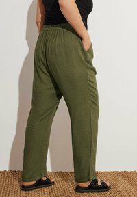 Olivgröna byxor i linneblandning med avslappnad passform, elastisk midja, sidofickor och uppvikta mudd, kombinerat med svarta sandaler.