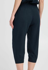 Pantalons capri bleu foncé en tissu léger, avec une taille élastique et des poignets froncés pour un ajustement décontracté.