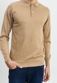 Beige lange mouw polo shirt gemaakt van lichtgewicht gebreide stof, met een klassieke kraag, een drieknopenlijst en ribbelboorden en -zoom.