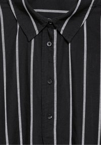 Chemise noire à boutons avec des rayures verticales grises, dotée d'un col classique et d'un tissu texturé. Deux boutons noirs sont visibles.