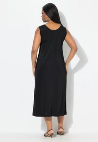 Mustat hihattomat mekko, jossa on pyöreä kaula-aukko, polvimittainen, valmistettu sileästä kankaasta, selkäpuolella halkio ja minimaalinen yksityiskohtaisuus.