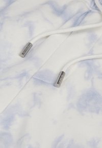 Hoodie i vitt med ljusblå tie-dye mönster. Har vita dragsnören med metallaglar. Mjuk tygtextur.