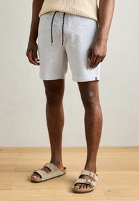 Men's lightweight, patterned swim shorts in white and grey, featuring an elastic waistband with drawstring and side pockets. Paired with beige sandals.