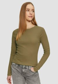Olivgrünes Langarmshirt mit gerippter Textur und rundem Ausschnitt, kombiniert mit grauen Jeans in schmaler Passform.