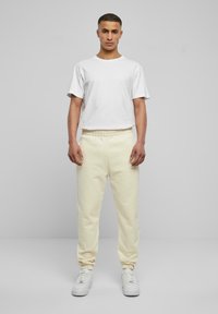 Beige sweatpants with elastic cuffs, paired with a white crew-neck t-shirt, worn with white sneakers. Simple, casual design.