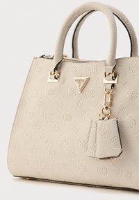 Borsa beige con texture e motivi in rilievo, doppi manici, ferrature tono oro e un accessorio staccabile simile a un portachiavi.