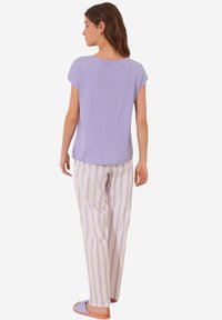 Lila kortemouwen top met een losse pasvorm, gecombineerd met crèmewitte gestreepte broek met paarse strepen, en paarse slippers. Zachte stoftextuur.
