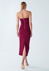 Brez naramnic bordo halja z oprijetim zgornjim delom, zadrgo na hrbtni strani in sprednjo režo, izdelana iz teksturiranega blaga; dolžina do polovice meč.