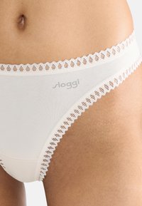 Beige bomuldsboksershorts med blomstret blondekant langs taljen. Har Sloggi-logo i lys grå på forsiden. Glat tekstur, fuld dækning.