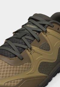 Nærbilde av en brun og olivengrønn tursko med meshpaneler, tykke lisser og forsterkede hull, som viser øvre front- og sidedetaljer.