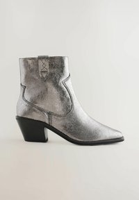 Bottines métalliques argentées avec un bout pointu, un petit talon empilé, une couture décorative, et une languette à l'arrière.