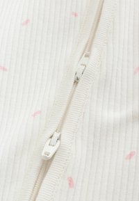 Gros plan sur un tissu blanc côtelé avec de petits points roses comportant deux curseurs de fermeture éclair blancs sur des pistes adjacentes.