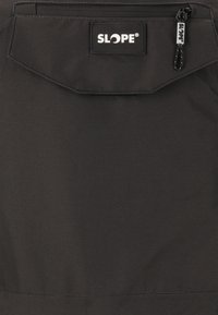 Schwarzer Rucksack mit einer vorderen Reißverschlusstasche und einem Klappenverschluss, versehen mit einem Etikett mit der Aufschrift "SLOPE" und einer strukturierten Stoffoberfläche.