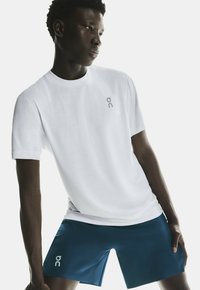 T-shirt blanc à manches courtes avec un petit logo gris sur la poitrine, associé à un short de sport bleu foncé arborant un logo contrastant.