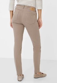 Beige Skinny Jeans mit fünf Taschen, einem Lederanschrieb und einer glatten Textur. Getragen mit flachen, hellbraunen Schuhen.