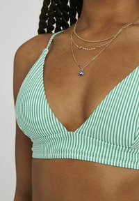 Haut de bikini rayé vert et blanc avec un décolleté en V profond, en tissu texturé et une bande ajustée. Colliers en or superposés avec un charme bleu.