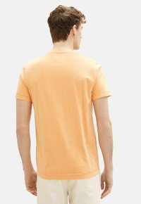 Kortærmet t-shirt med rund hals i lys orange bomuldsstof, med en glat tekstur og et enkelt design, set fra ryggen.