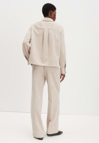 Giacca di velluto a coste beige e pantaloni coordinati, con una trama a coste verticali. La giacca presenta una piega sul retro e una silhouette sartoriale.