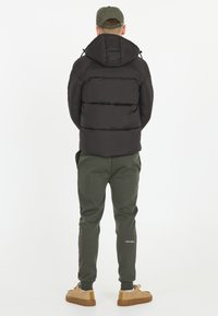 Svart puffjacka med huva, med en kviltad design. Kombineras med gröna joggingbyxor och bruna sneakers med gummisula.