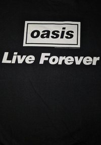 Sort t-shirt med hvid trykt tekst: "oasis" i en ramme oven over "Live Forever." Stoffet har en glat, ensartet tekstur.