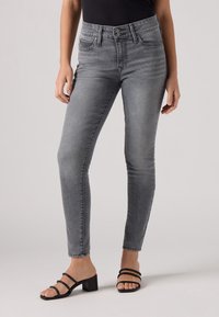 Pantalones vaqueros ajustados grises de mezclilla con cintura alta, que presentan un diseño clásico de cinco bolsillos y un ligero desvanecimiento, combinados con sandalias negras de tiras.