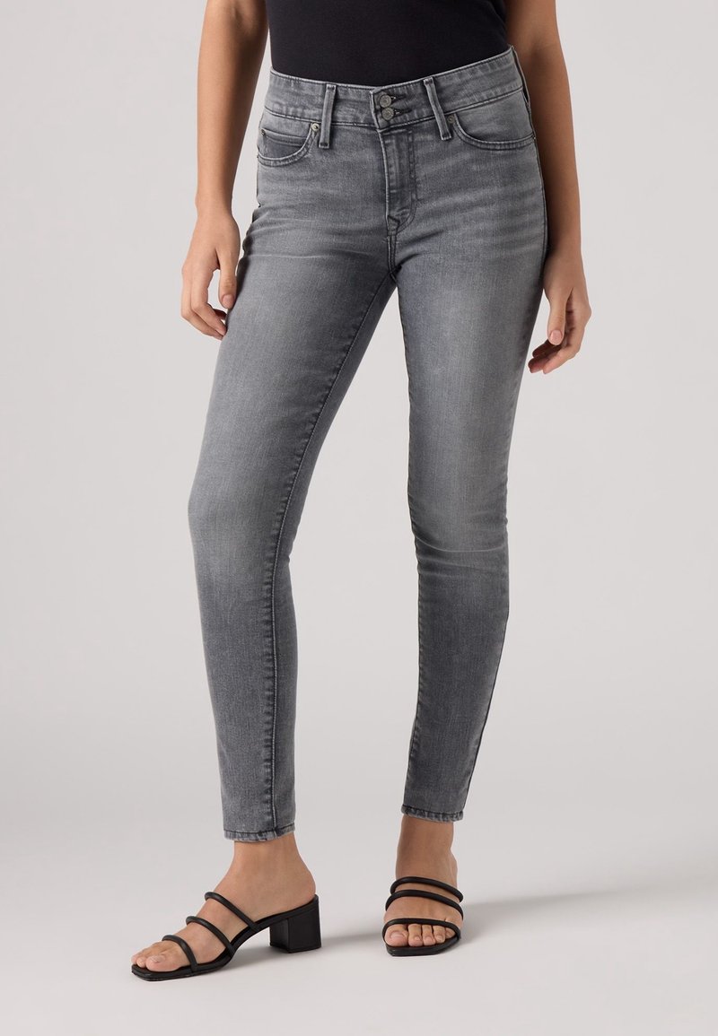 Pantalones vaqueros ajustados grises de mezclilla con cintura alta, que presentan un diseño clásico de cinco bolsillos y un ligero desvanecimiento, combinados con sandalias negras de tiras.